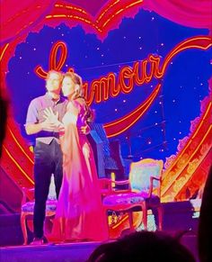 a man and woman standing on stage in front of a heart shaped sign with the word love