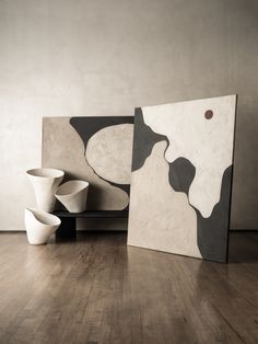 two white vases sitting on top of a wooden floor next to an abstract painting