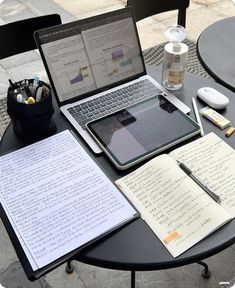 two laptops are sitting on a table with notebooks and pens