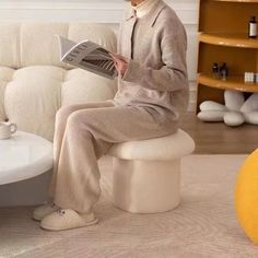 a woman sitting on a white couch reading a magazine