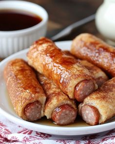 sausage wrapped in bread on a plate next to dipping sauce and a glass of ketchup