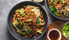 three bowls filled with noodles and meat on top of a wooden tray next to sauces