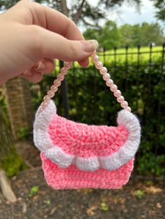 a hand holding a pink and white crocheted purse with pearls on the handle