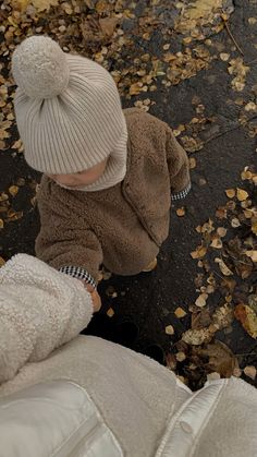 a small child wearing a white hat and coat looking down at leaves on the ground