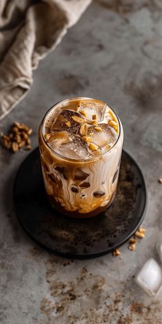 an iced drink on a black plate next to ice cubes and spoon with nuts