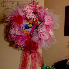 a pink and red wreath hanging on the wall next to a shelf with other items