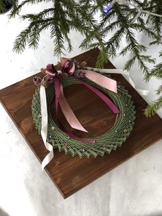 a christmas wreath on top of a cutting board next to a pine branch and ribbon