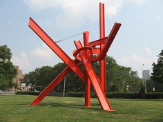 a large red sculpture sitting on top of a lush green field