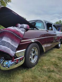 an old car with a blanket on it's hood sitting in the grass near other cars