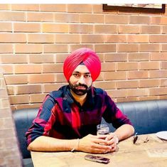 a man with a red turban sitting at a table in front of a brick wall