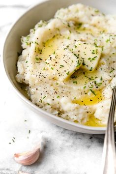 a bowl filled with mashed potatoes topped with butter and seasoning next to garlic