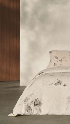 an old photo of a bed with white sheets and floral designs on it, in front of a wood paneled wall