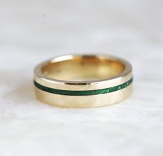 a close up of a wedding ring on a white surface with green and gold stripes