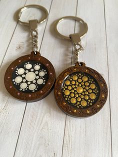 two brown and black keychains with gold dots on the bottom one has a circular design