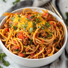 a white bowl filled with spaghetti topped with ground beef and cheese, garnished with cilantro