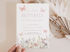 a person holding up a butterfly birthday party card with flowers and feathers in the background