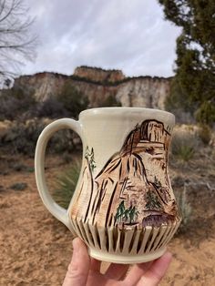 a hand holding a coffee cup with a mountain scene on it