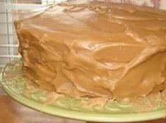 a chocolate cake with frosting sitting on top of a green plate in front of a window