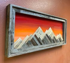 a painting hanging on the side of a wall next to a wooden frame with mountains painted on it