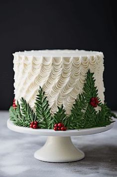 a white frosted cake decorated with evergreen leaves and berries