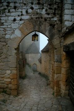 an alley way with stone walls and cobblestone pavement, leading to two buildings