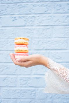 a hand holding a stack of macaroons in front of a blue brick wall