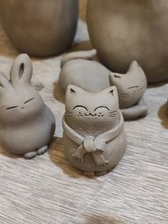 several clay cats sitting on top of a wooden table next to vases and bowls