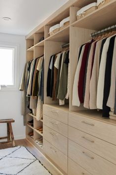 an organized closet with clothes hanging on wooden shelves and drawers in front of a window