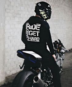 a man sitting on the back of a motorcycle wearing a helmet and riding it in front of a brick wall