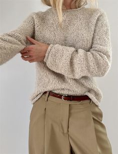 a woman wearing a sweater and pants with her hands in her pockets, standing against a white background