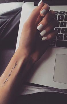 a woman's hand with a small tattoo on her left wrist, next to a laptop