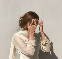 a woman covers her face with her hands as she stands in front of a wall