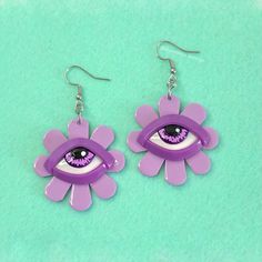 two pairs of purple earrings with an eye in the center on a green background,