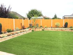 a backyard with artificial grass and wooden fenced in areas that include trees, shrubs, and flowers