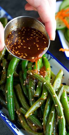 someone is dipping sauce on green beans in a blue and white plate with other dishes