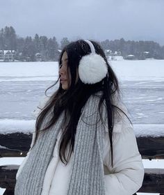 a woman standing in the snow next to a bench with ear muffs on her head