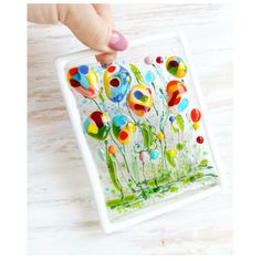 a hand is holding a glass painting on a white plate with flowers in the middle