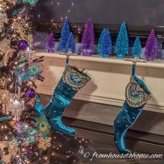 blue christmas stockings hanging from a fireplace mantel next to a tree with purple and green decorations