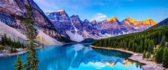 a lake surrounded by mountains and trees with blue water in the foreground, on a sunny day