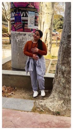 a woman standing next to a tree in front of a newspaper dispenser