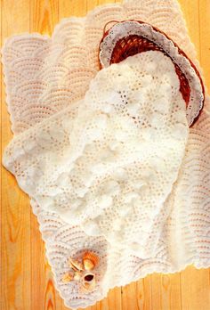 a white crocheted blanket on top of a wooden floor next to a basket and seashells