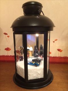 a lantern with snow and trees in it on a wooden table next to a wall