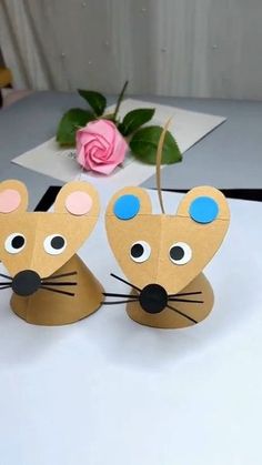 two paper mouses sitting on top of a table next to a pink rose and a vase