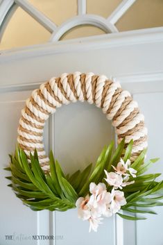 a diy coastal wreath with flowers and rope hanging on the front door for an easy summer decor idea