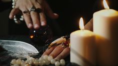 a person holding a wine glass in front of two candles and pearls on a table