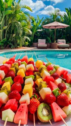 fruit skewers sitting on top of a white plate next to a swimming pool