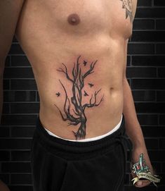 a man with a tree tattoo on his stomach is standing in front of a brick wall