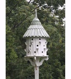 a white bird house sitting on top of a wooden pole in front of some trees