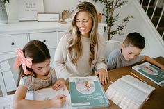 a woman sitting at a table with two children and an open book in front of her