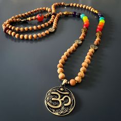 The Chakra Colors Yoga Mala Beaded Necklace is a spiritual and meaningful piece of handmade jewelry that combines natural elements and powerful symbolism. This unique necklace is commonly used in meditation and yoga practices to enhance the spiritual experience and promote a sense of balance and harmony.The handmade necklace is made with natural sandalwood beads, which are known for their calming and soothing properties. Sandalwood has been used for centuries in various spiritual practices to he Spiritual Wooden Beads Jewelry For Meditation, Holistic Necklaces With Wooden Beads For Festivals, Holistic Festival Necklaces With Wooden Beads, Spiritual Wooden Beads Necklace For Meditation, Spiritual Wooden Beads Mala For Festival, Spiritual Wooden Beads Jewelry For Healing, Meditation Amulet With Wooden Beads, Wooden Beads Amulet Jewelry For Meditation, Holistic Mala With 108 Beads For Festival